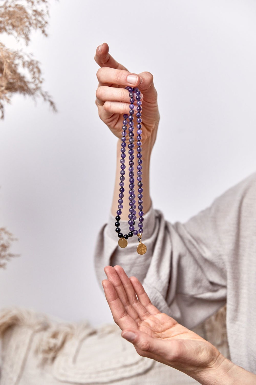 PEACE OF MIND Mala aus Amethyst und schwarzen Turmalin Steinen mit goldenen NAIONA Plättchen und Perlen. Mood, Pose, Hemd, Hände, Decken, Kissen, Trockenblumen.