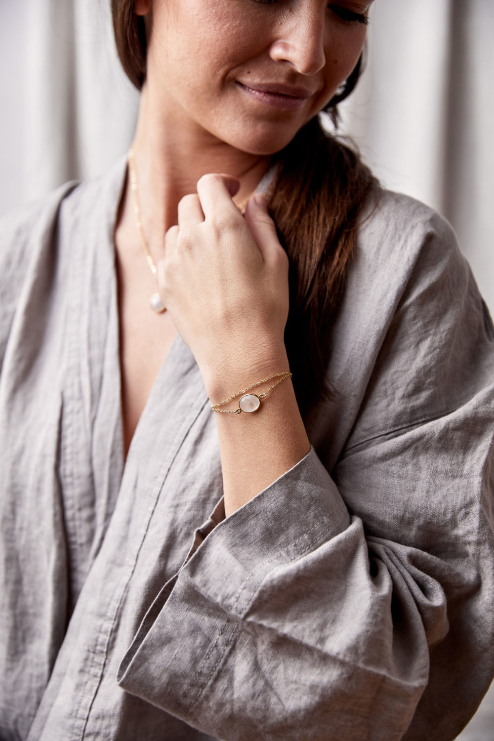KAUPO Armband gold mit Mondstein weiß und goldenem NAIONA Plättchen und KAUPO Kette gold. Pose, Frau, Hand, Handgelenk, Bluse.